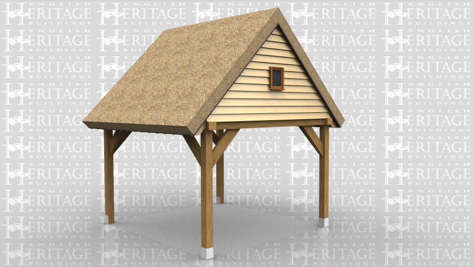 This oak frame is an open carport attached to an existing building on one side. The roof has a gable end and the roof covering is thatch. The gable is weatherboarded and has a small window in it.