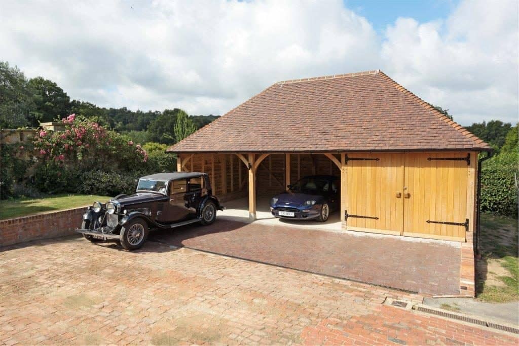 An oak framed garage with two luxury cars parked inside it