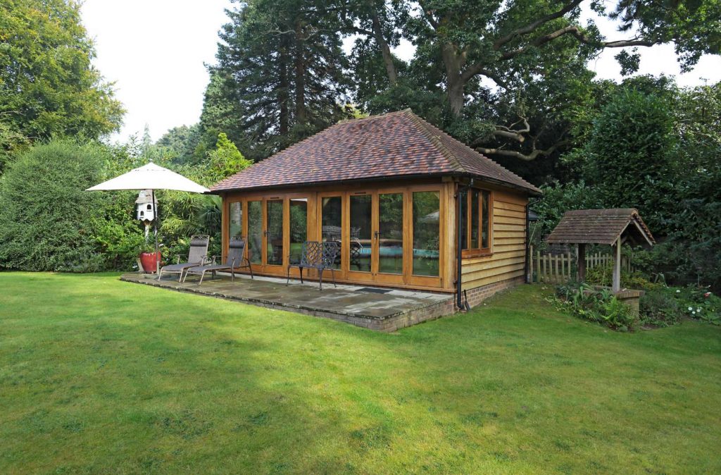 An oak framed garden room with a patio on a well-kept lawn
